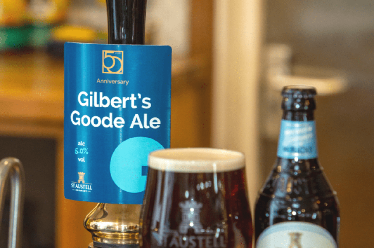 Close-up of a brewery pump with a pump card displaying the name ‘Gilbert’s Goode Ale,’ created as a tribute to the event. A pint of beer, and a beer bottle sit on the bar displaying the actual branding.