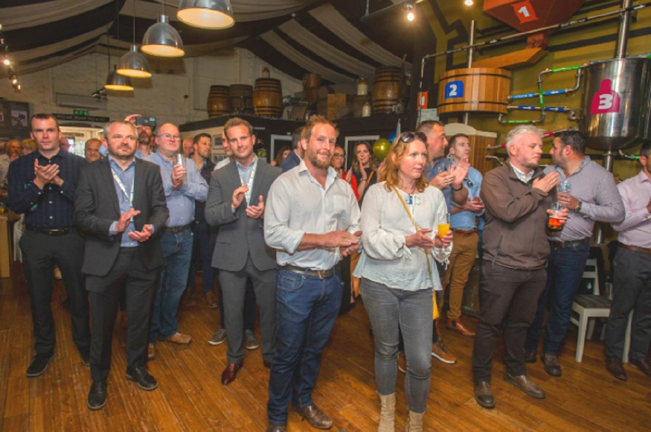 A crowd of event attendees enjoying speeches from the management team at Gilbert & Goode, with happy faces clapping in appreciation.