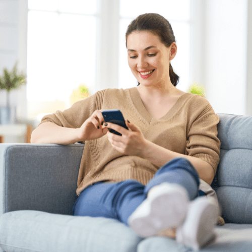 A smiling lady sat on a sofa with her legs crossed looking down at her phone