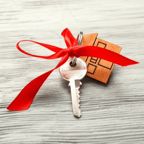 A key with a red ribbon and wooden house keychain attached to it