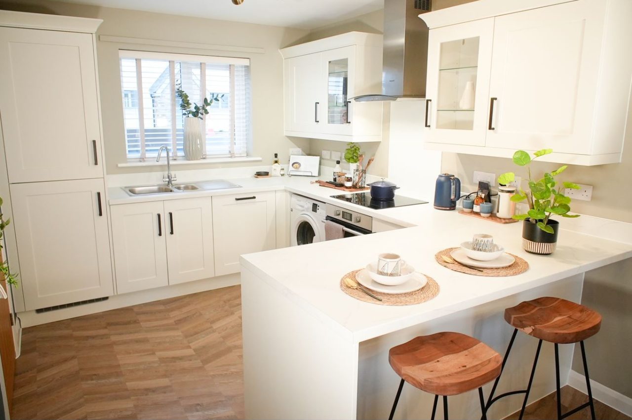 A modern kitchen area with white counter tops and cupboards and a wooden floor